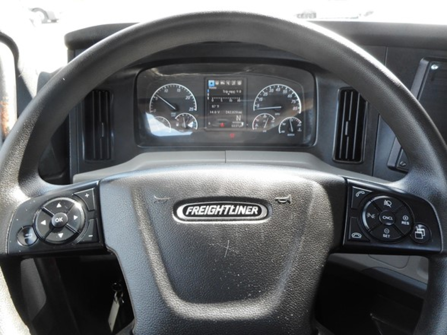 Dashboard and steering wheel of a Freightliner Cascadia day cab showing instrument cluster, steering wheel with Freightliner emblem, and control stalks.