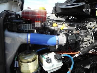 Freightliner Cascadia 126 engine bay showing coolant reservoir, power steering reservoir, and blue hose connected to intercooler or intake pipe.