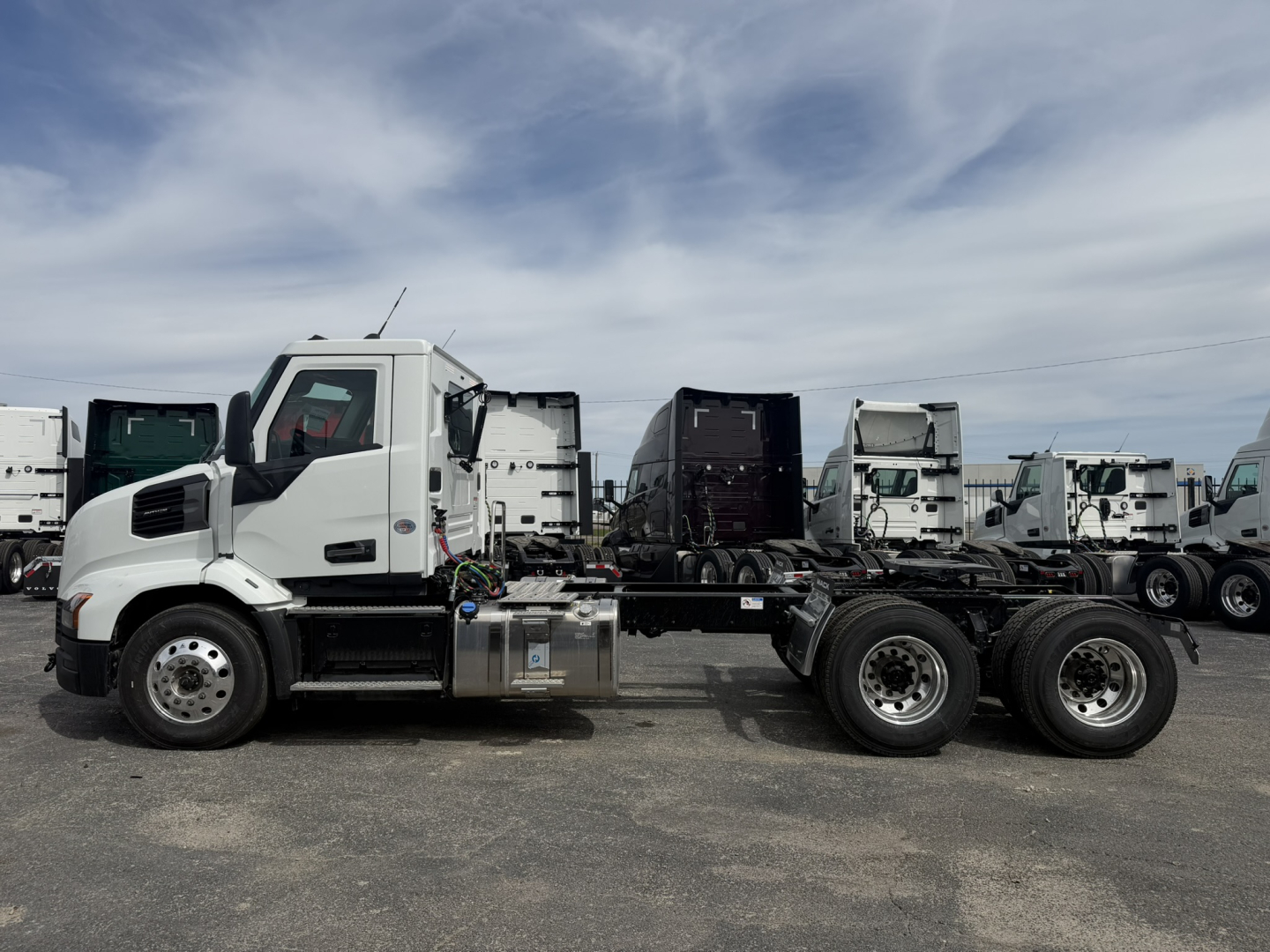Truck chassis with cab in foreground and multiple white trucks in background.