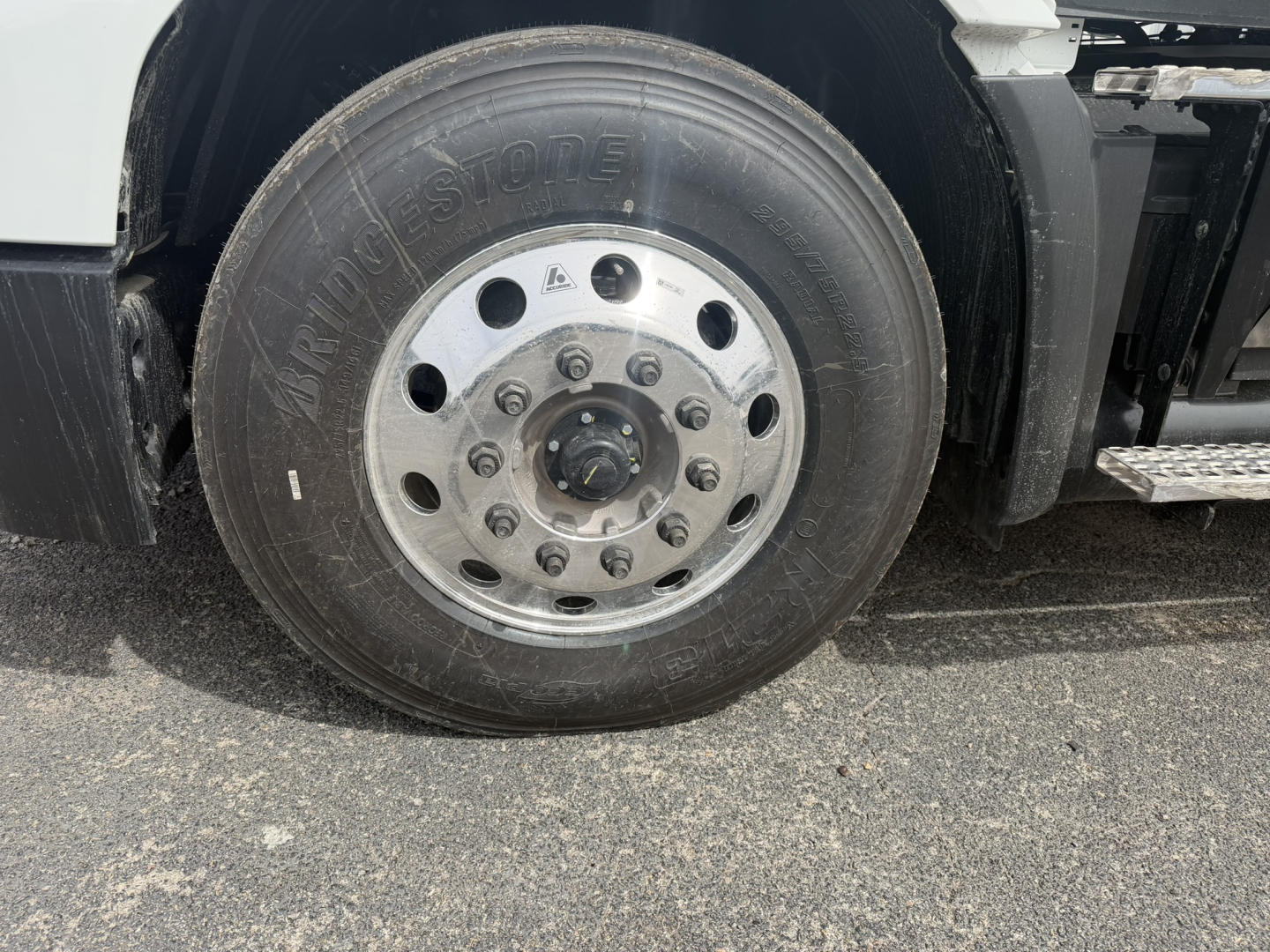 Front wheel of a new Mack AN64T daycab showing Goodyear/Bridgestone tire and polished aluminum wheel with lug nuts.