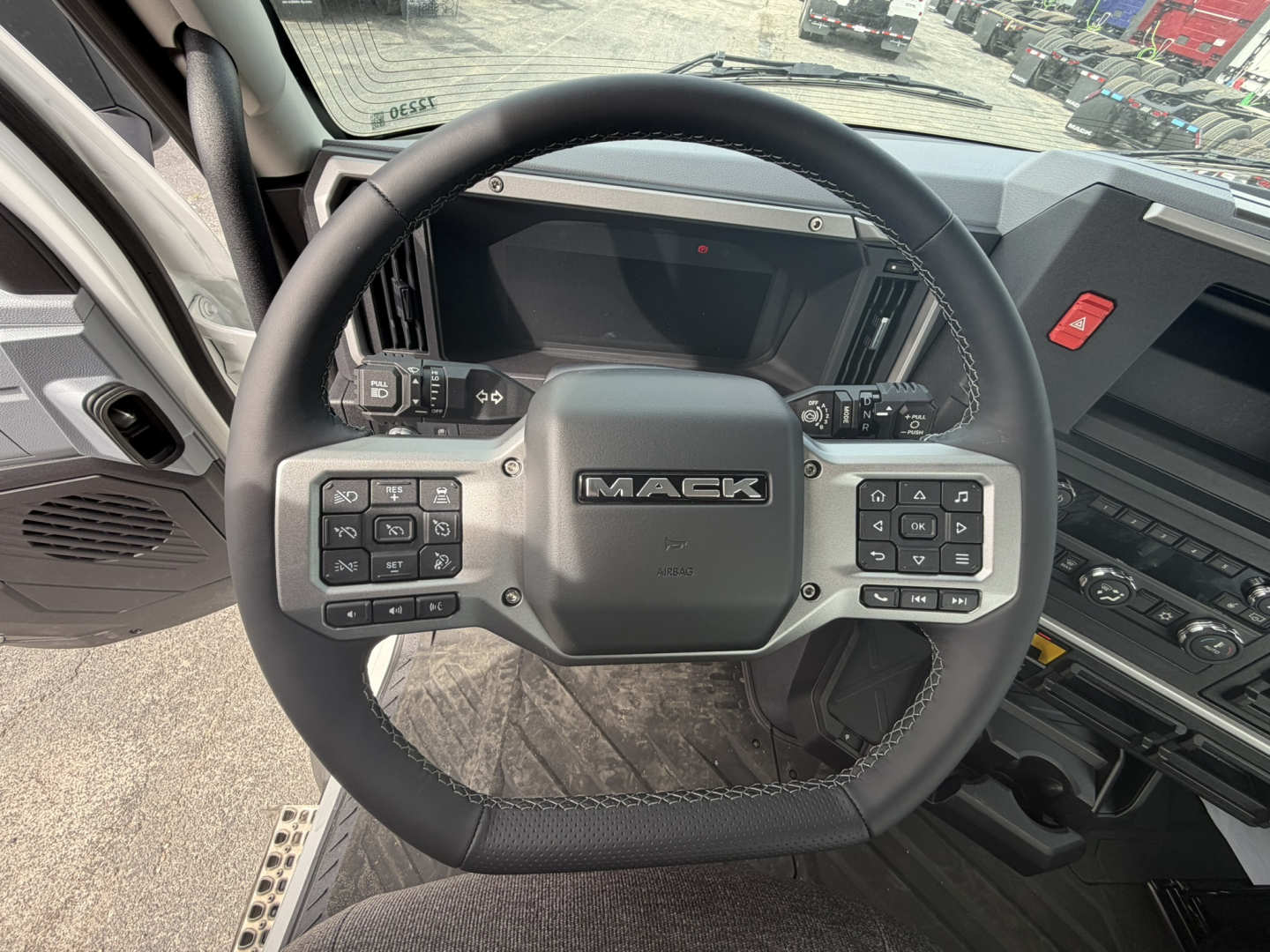 Mack AN64T truck interior showing steering wheel with Mack logo and multifunction buttons, digital dash, and center console from driver’s perspective.