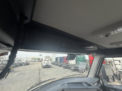 Truck cab interior view with overhead storage and control panel, windshield showing a truck lot with other vehicles.