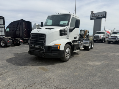Truck front-left view showing Mack AN64T cab chassis with white exterior, grille, headlights, and Mack logo. Visible text includes 'MACK' on grille and 'MACK' sign in background.