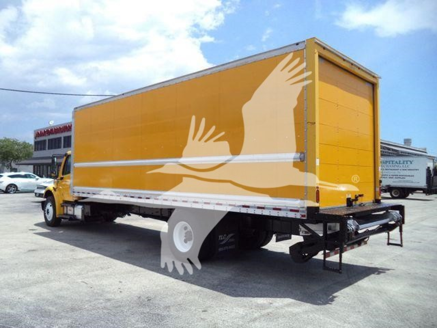 Yellow Freightliner M2 106 box truck with side graphics, rear view showing cargo box and ramp, no visible text other than generic markings.