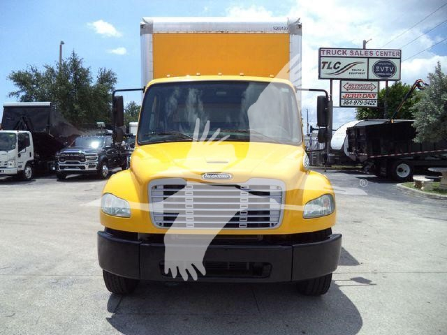 Front view of a yellow 2019 Freightliner M2 106 box truck showing the cab and cargo box, with dealership signs in the background.