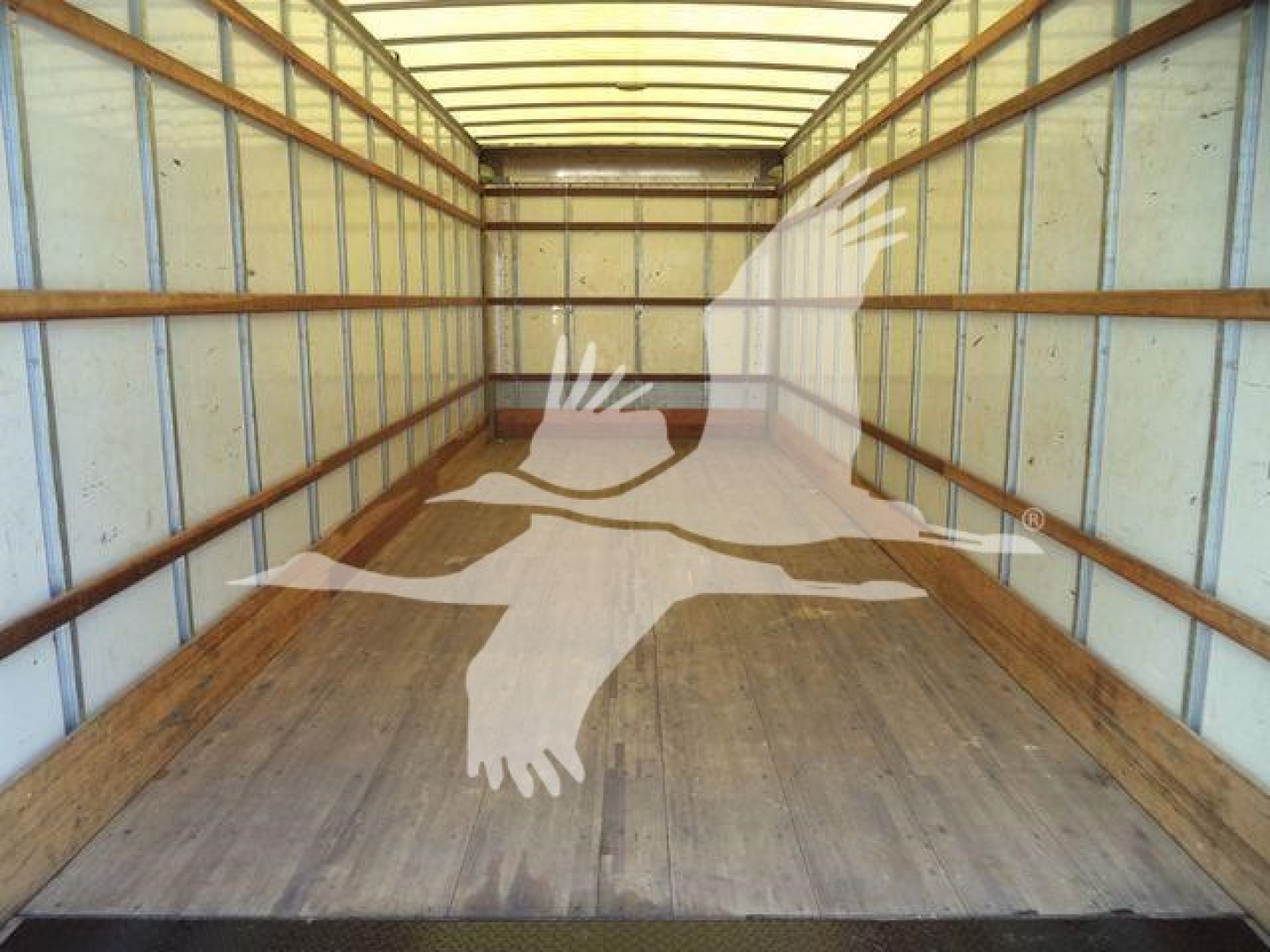 Interior of a Freightliner M2 106 box truck trailer with wooden floor and metal walls, showing a watermark of a flying eagle.
