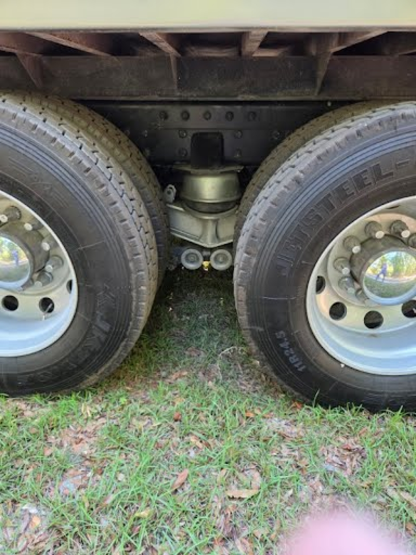 Dual rear truck tires with suspension hanger and leaf spring undercarriage center showing axle components.