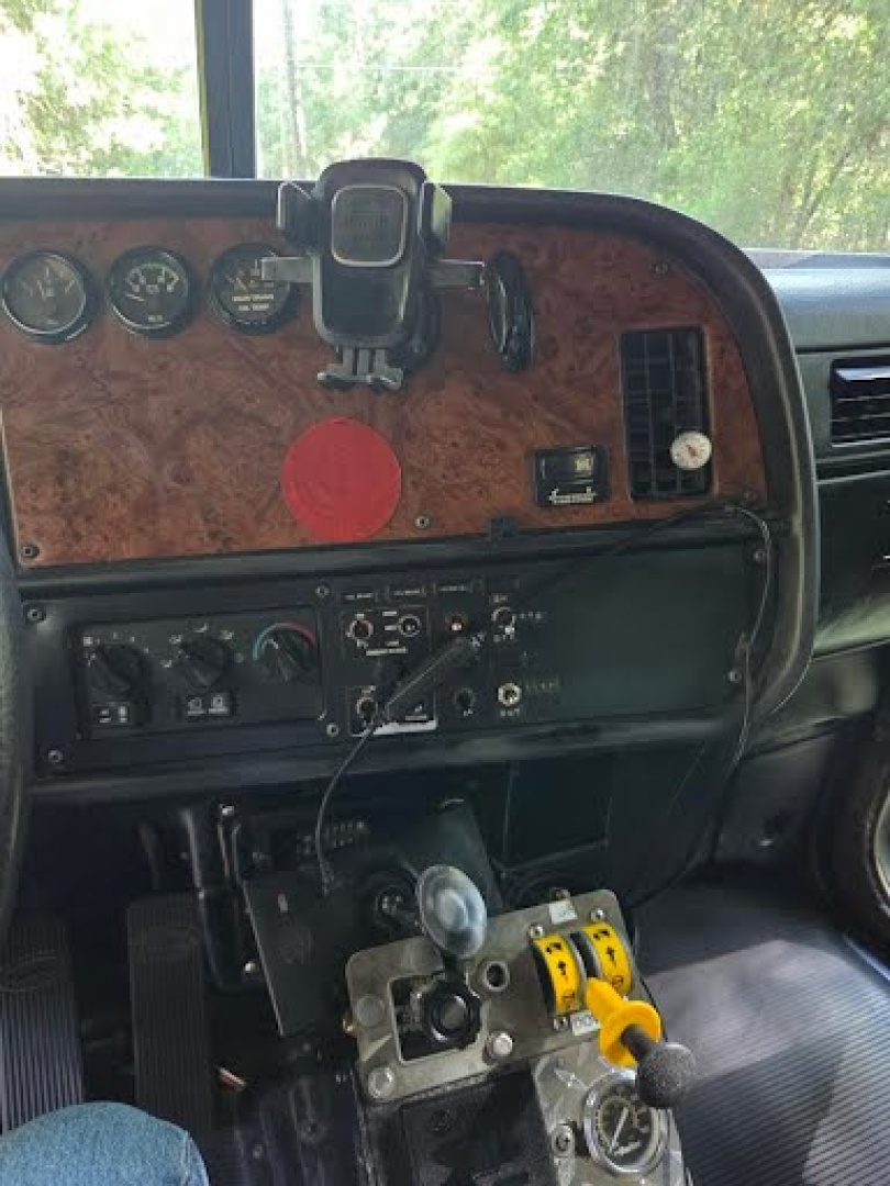 Peterbilt truck cabin dashboard with wood veneer panel, gauges, and a gear shifter in view.