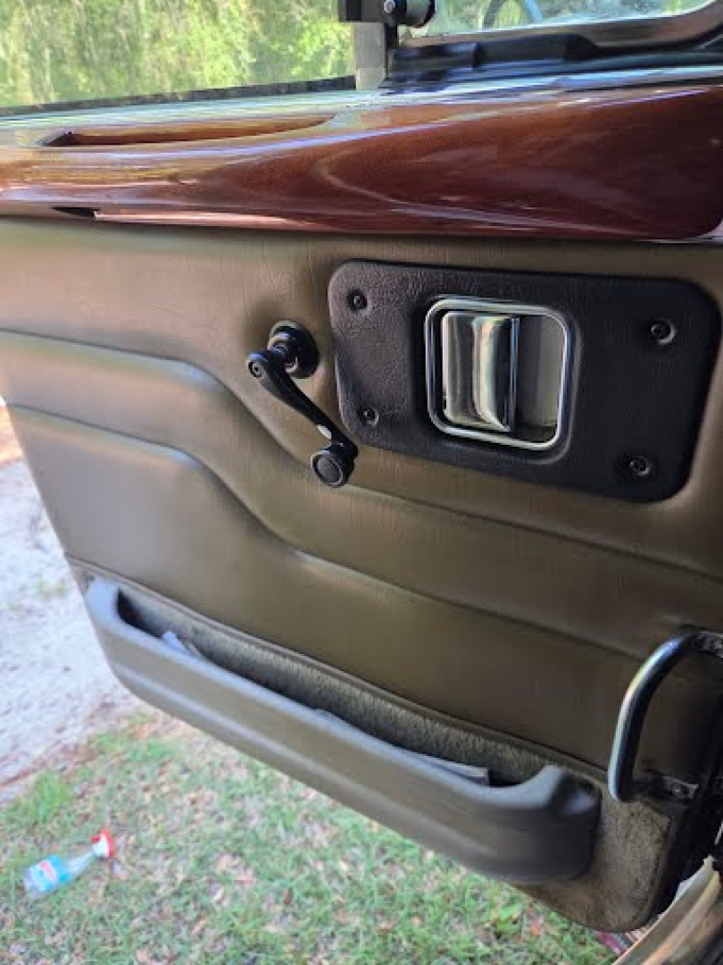 Truck door interior showing manual window crank, door handle, and beige paneling with wood trim on top.