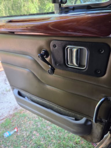 Truck door interior showing manual window crank, door handle, and beige paneling with wood trim on top.