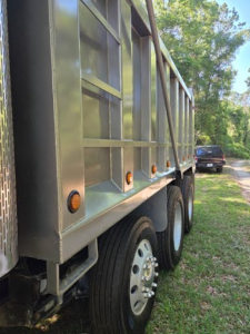 Dump truck side showing dual rear wheels and metal dump bed with orange reflectors