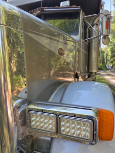 Peterbilt 378 hood and headlight area with chrome grille, large side mirror, and amber turn signal on the fender; chrome accents and polished metal surfaces visible.
