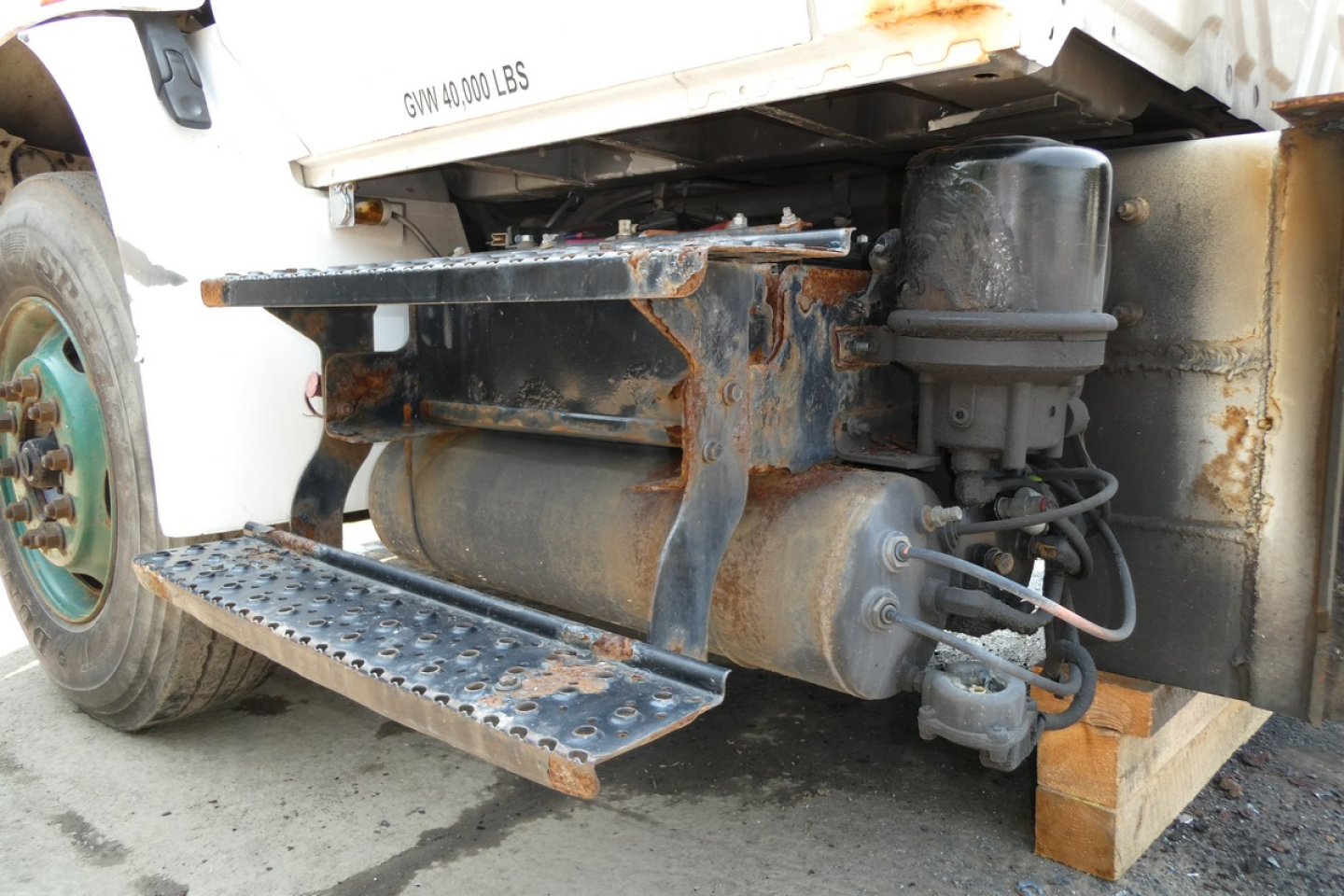 Truck drivetrain underside showing hydraulic/hosen components, steel step, and rusted frame on a 2005 International 4300 beverage truck.