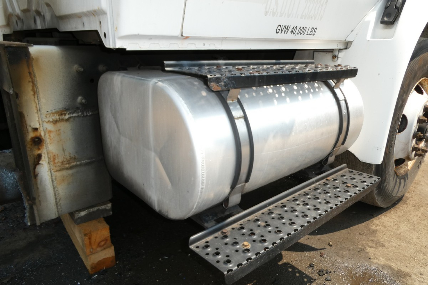 Truck fuel tank and side step under a 2005 International 4300 with visible aluminum tank and perforated metal step
