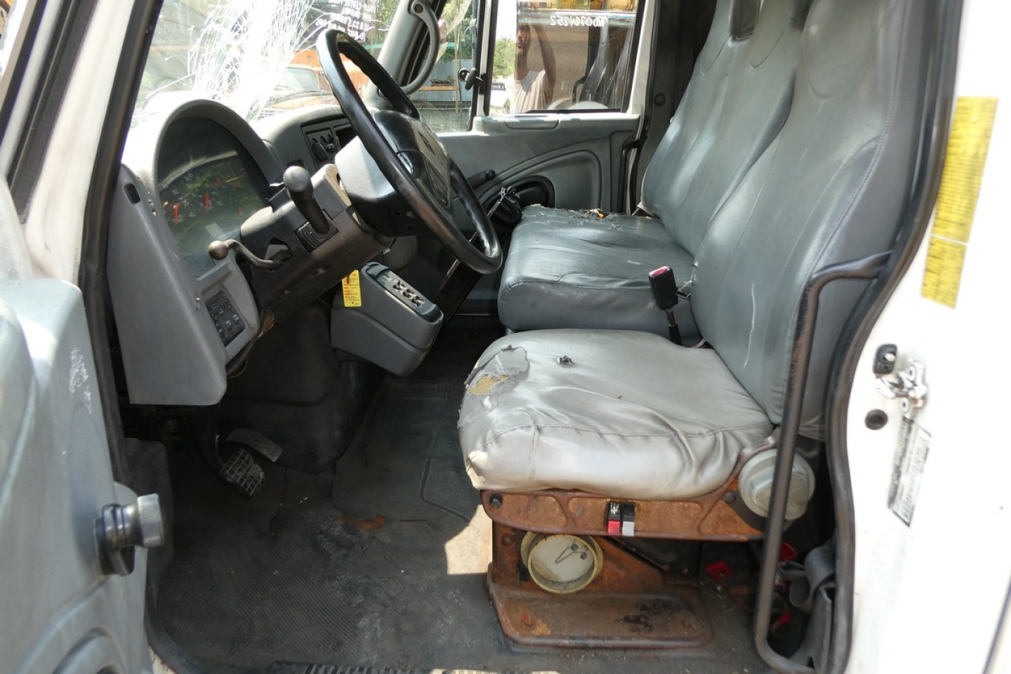 Truck cab interior showing driver seat and bench seat with worn cover, steering wheel, and dashboard in a beverage truck.
