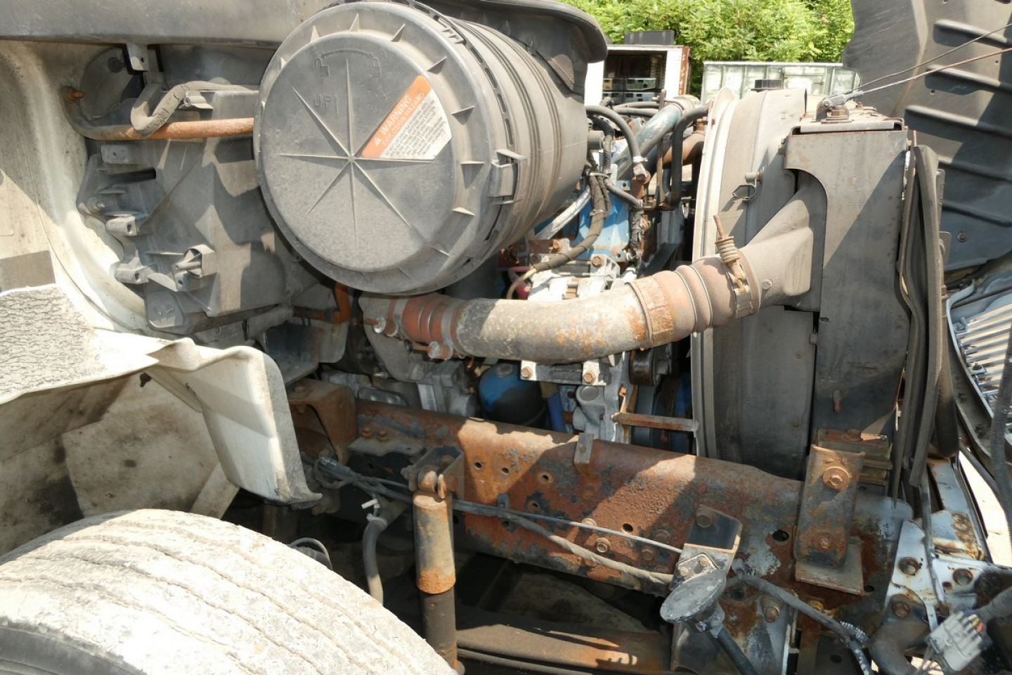 Engine bay of a 2005 International 4300 showing air filter canister, intake piping, radiator area, and rusted support brackets.