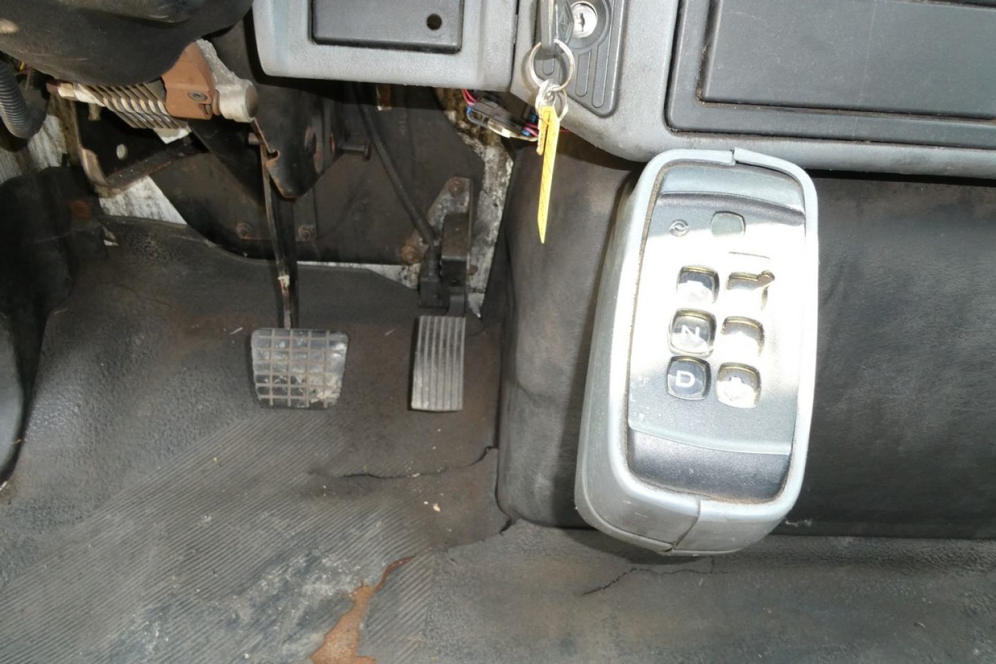 Truck pedal area showing clutch and accelerator pedals with a keypad drive control module mounted to the right under the dashboard, and a set of ignition keys in the ignition switch.