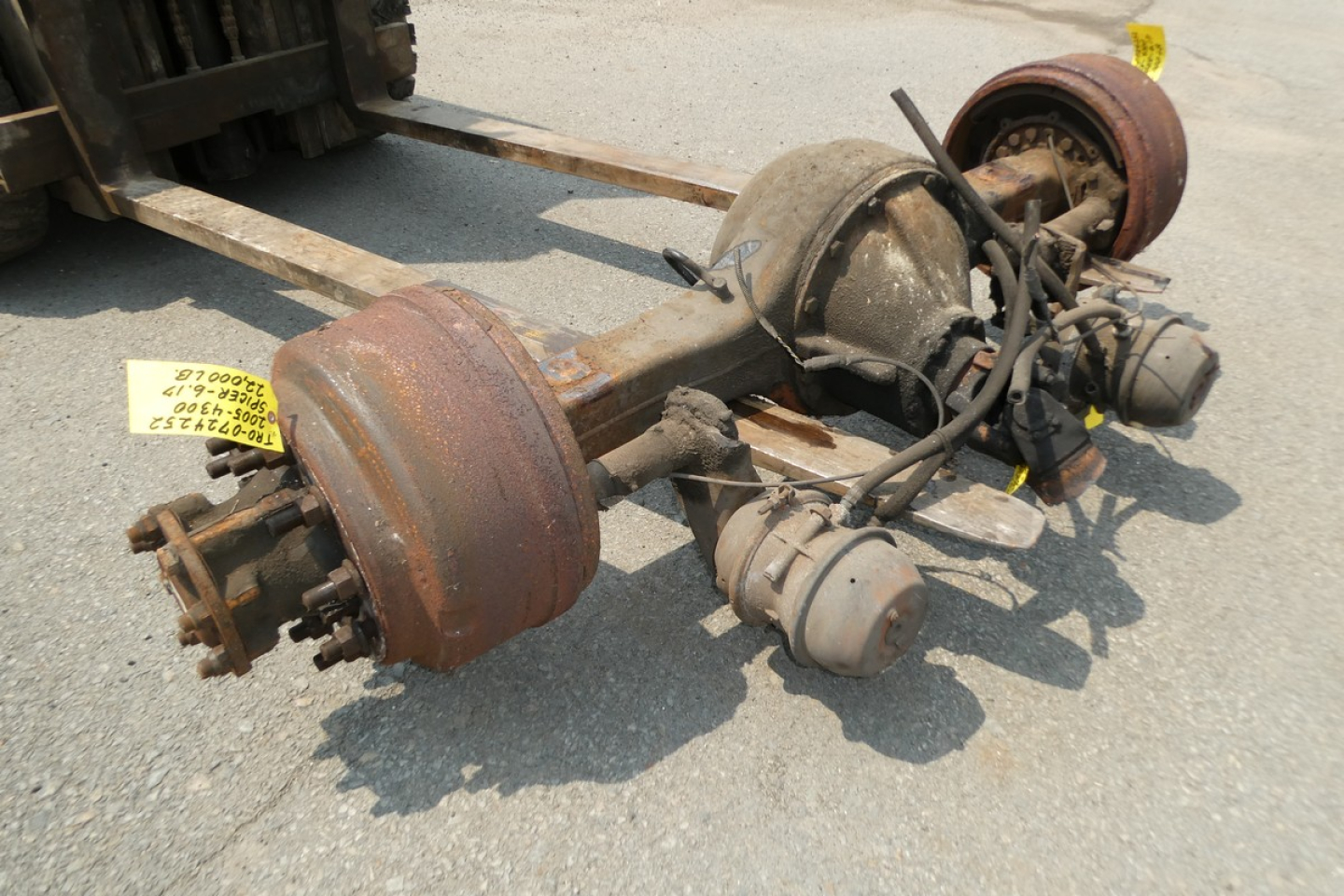 Truck rear axle assembly with brake drums and suspension components on the ground, rust-stained drums, air hoses, and differential housing visible.