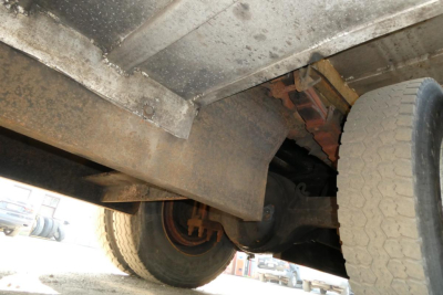 Underneath view of a 2005 International 4300 truck showing the front and rear suspension, axle housing, and a tire; rust and grime on metal components visible.