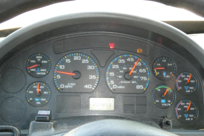 Dashboard of a medium-duty truck showing speedometer, tachometer, and auxiliary gauges, with warning lights and VIN plate visible.