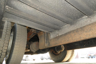 Truck undercarriage showing frame rails, axle, and suspension components with tire visible.