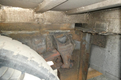 Truck chassis undercarriage showing suspension hanger and leaf spring mounting with rust-colored metal components and a tire partial view.