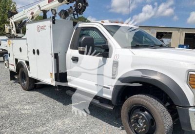 Ford F-550 utility service truck showing utility body with mounted boom crane and wheel. Visible text on service body including company logo and labels.