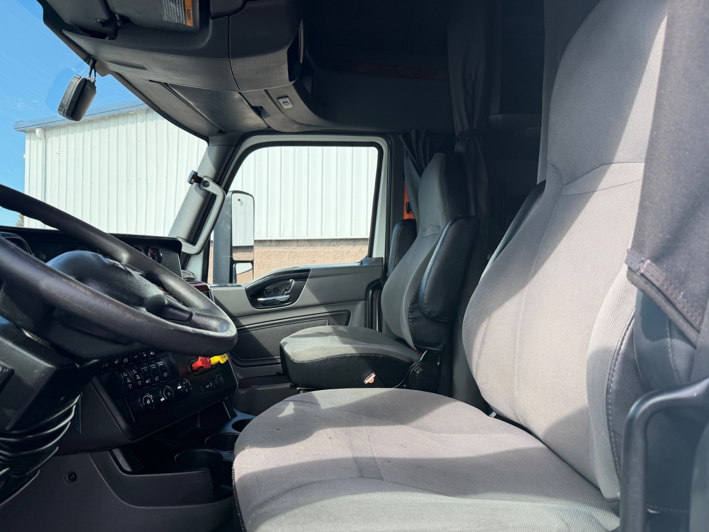 Interior of a 2021 International LT625 truck cab, driver seat and passenger seat visible with steering wheel, dashboard, and side window; light gray upholstery.