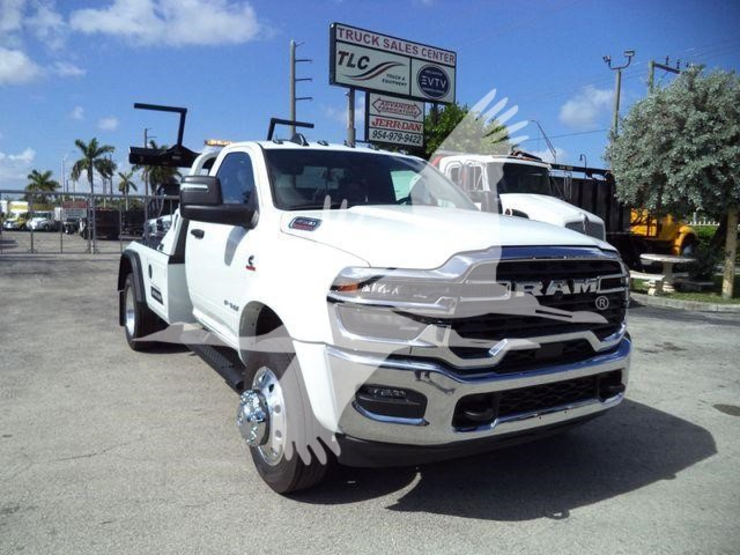 Ram 4500 tow truck in white with front chrome grille and dual rear wheels, dual front wheels removed revealing hubs, tow equipment in background, dealership lot