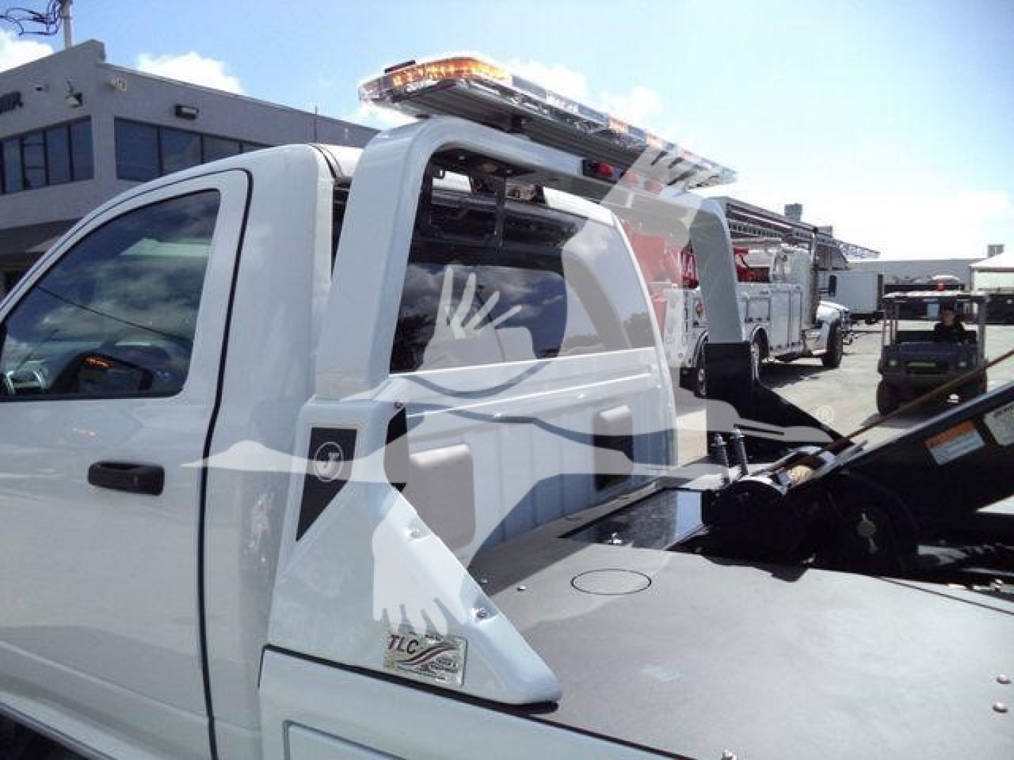 Ram 4500 pickup with winch equipment in a dealership lot, white cab, rear bed setup with roll bar and light bar on top.