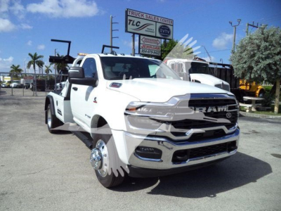 Ram 4500 tow truck in white with front chrome grille and dual rear wheels, dual front wheels removed revealing hubs, tow equipment in background, dealership lot