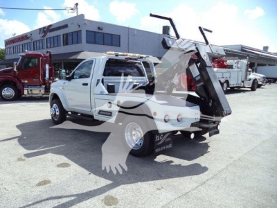 White Ram 4500 pickup with a large folded hydraulic tow/winch bed in a dealership lot; background shows a white building with windows and other trucks.