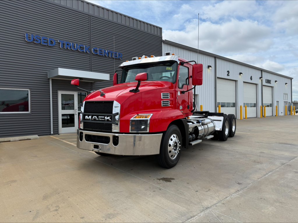 Mack AN64T conventional daycab truck in red with chrome front bumper, parked outside Used Truck Center; visible text includes 'MACK' on grille, 'USED TRUCK CENTER' on building, and signage on the truck’s side windows.