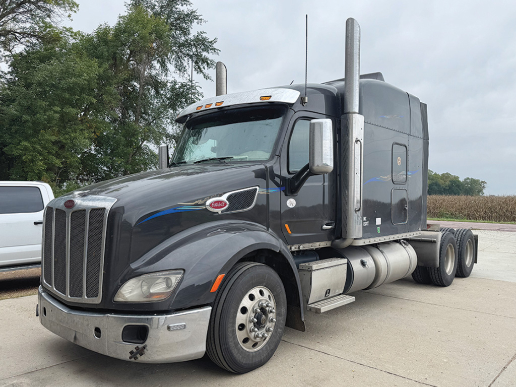 Peterbilt 579 UltraCab tractor in a dark gray color, front and side view, with tall exhaust stacks, chrome bumper, and dual rear axles; cab details visible.