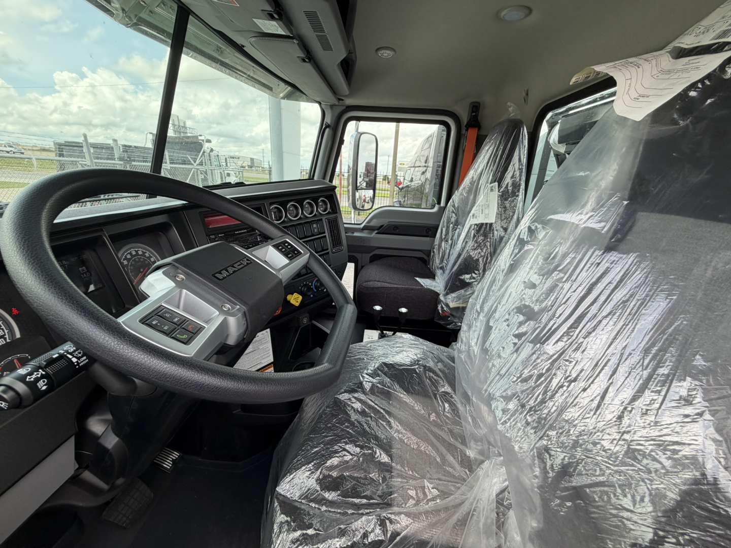 Cab interior of a new 2026 Mack GR64B rolloff truck showing steering wheel, dashboard, and plastic-covered seats.