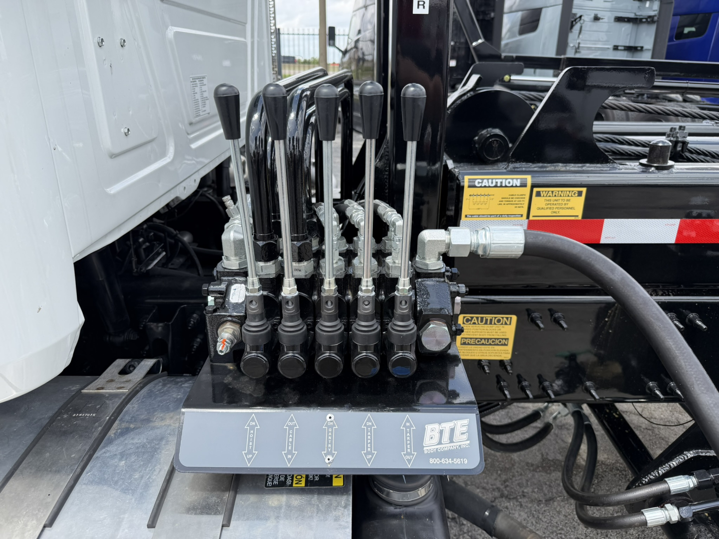 Control lever panel with eight hydraulic levers and control block on Mack GR64B roll-off truck showing hydraulic lines and gauges.