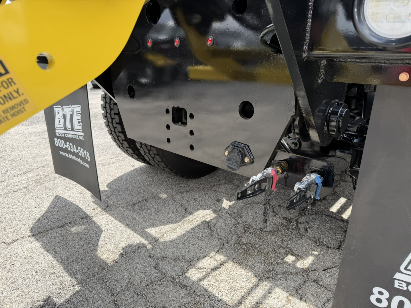 Rear view of a 2026 Mack GR64B roll-off truck showing side-mounted connectors and chassis panel with warning label.