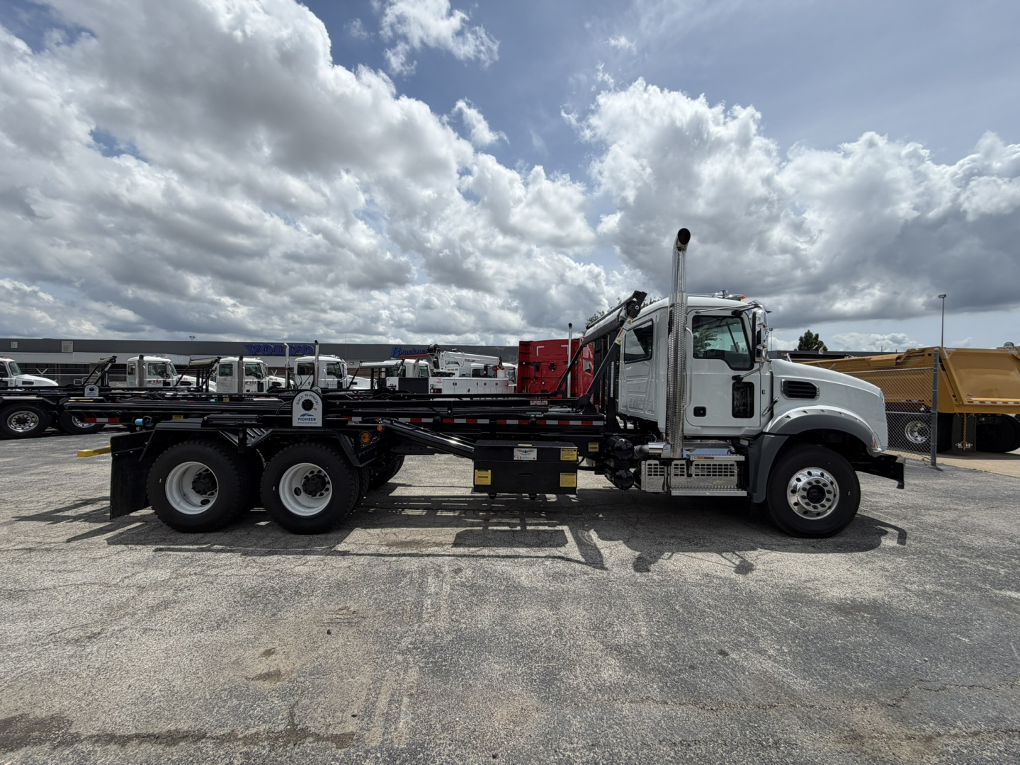 Side view of a 2026 Mack GR64B roll-off truck showing long flatbed with hydraulic arms and cab, VIN visible in listing, no visible text on components.