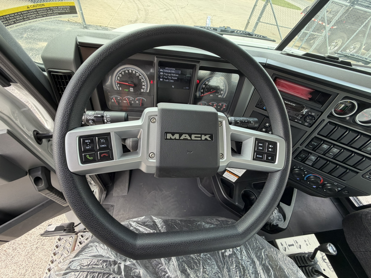 Wheel steering wheel and dashboard of a Mack GR64B truck cab with instrument cluster and controls visible.