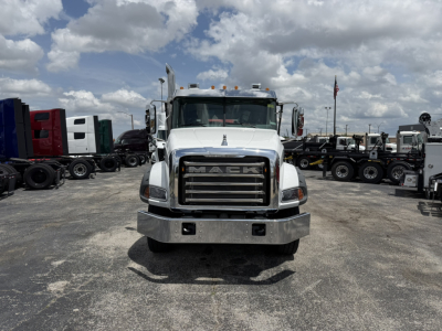 Front view of a white 2026 Mack GR64B truck in a lot, with grille reading MACK, large bumper, headlights, dual exhaust stacks, and other trucks in background.