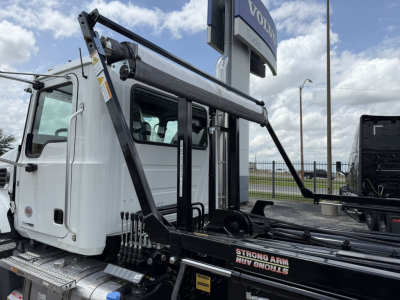 Mack GR64B truck in white cab with roll-off hoist and Strong Arm hook lift system, side view showing hydraulic arms and controls.