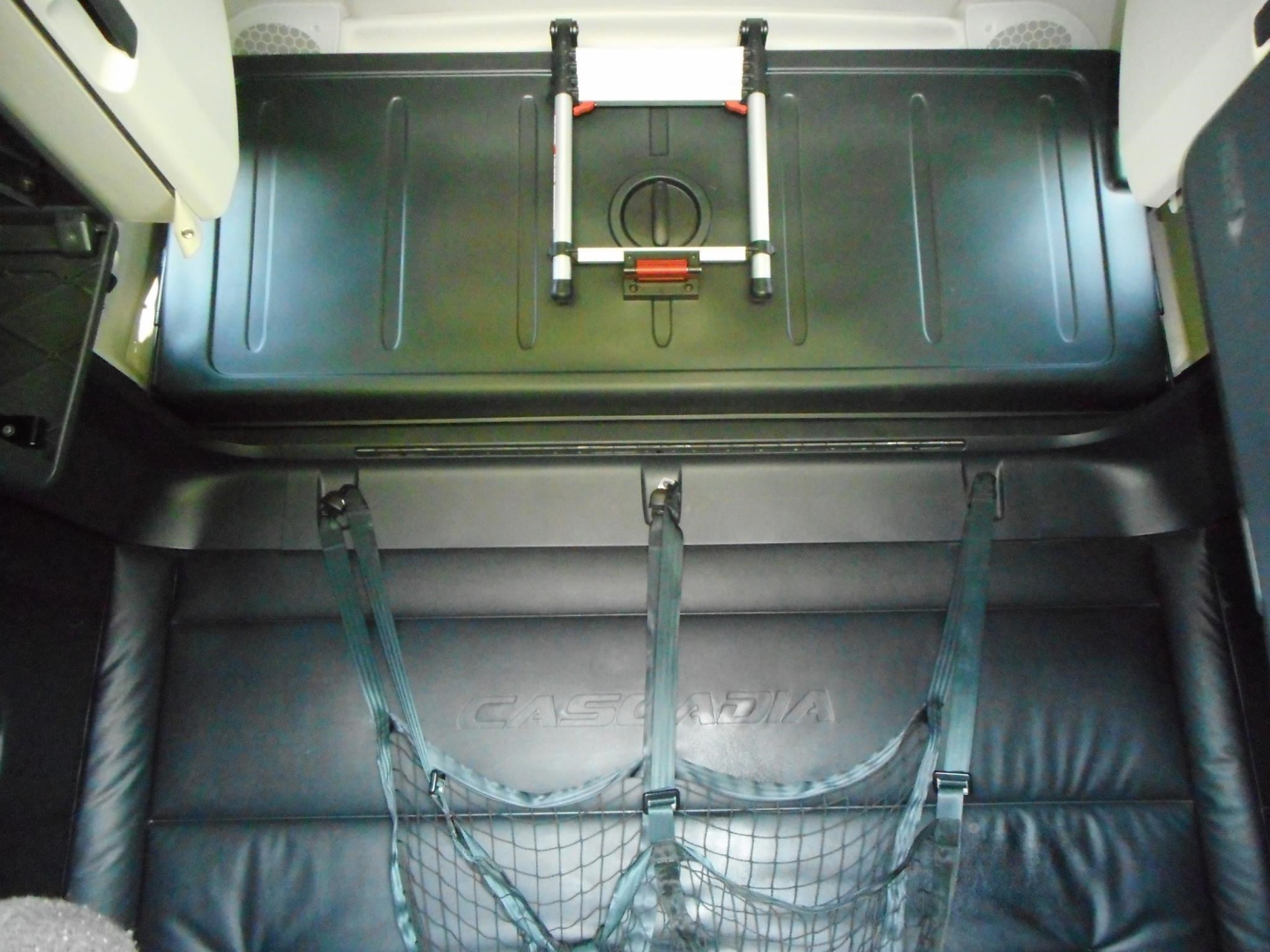 Freightliner Cascadia 126 cab interior showing cargo area with latching strap anchor and netting, black leather seat/back area with embossed Cascadia logo.