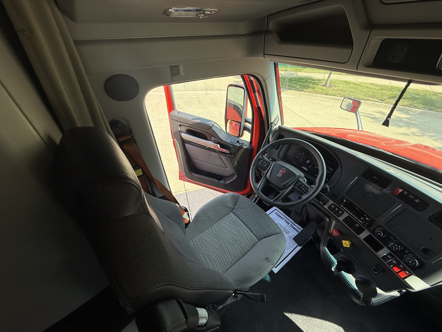 Truck cab interior of a 2024 Kenworth T680 with steering wheel, dashboard, and driver seat visible.