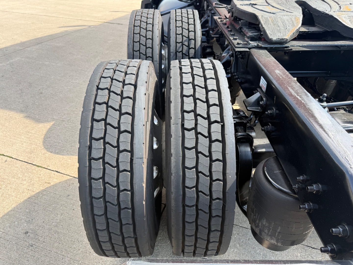 Dual rear axles with tires next to a Kenworth chassis showing a cylindrical air tank and frame, undercarriage visible.