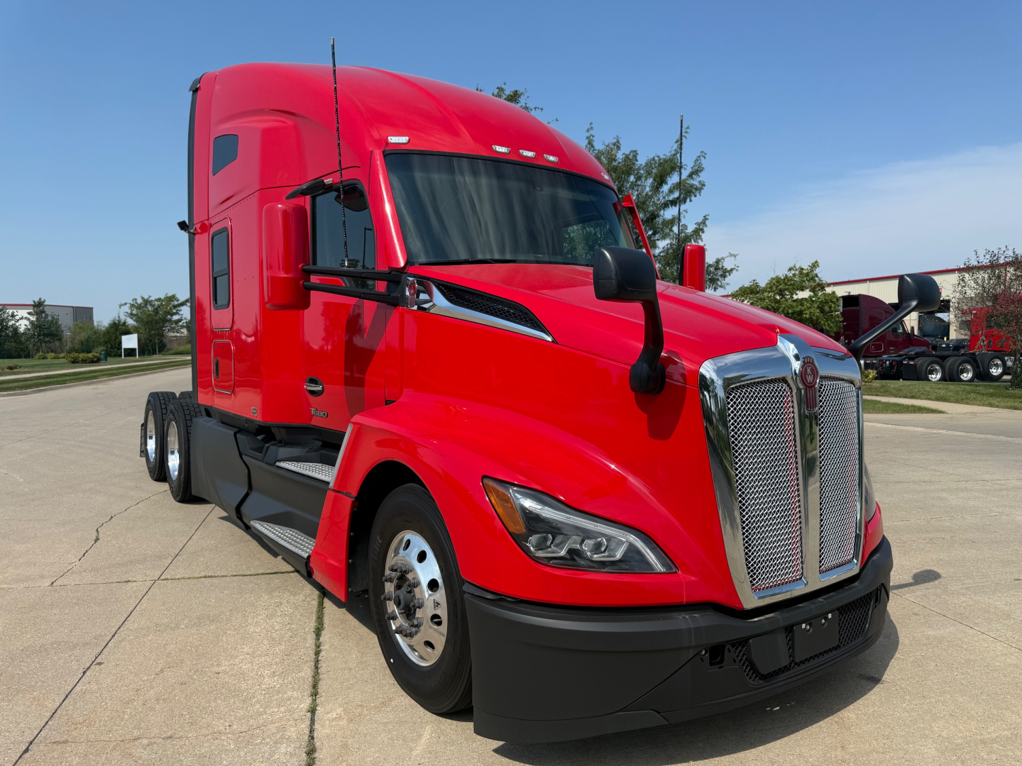 Kenworth T680 conventional sleeper truck in red, front three-quarter view showing chrome grille, headlights, and side mirror.