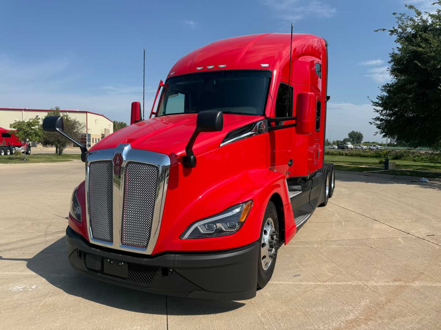 Kenworth T680 cab over view showing front grille and red exterior with black bumper and mirrors.
