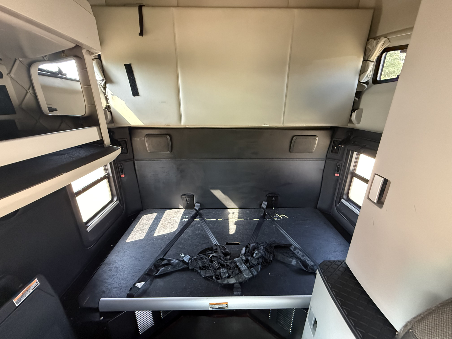 Truck cabin interior of a 2024 Kenworth T680 sleeper showing sleeping area with seat belts and storage compartments.