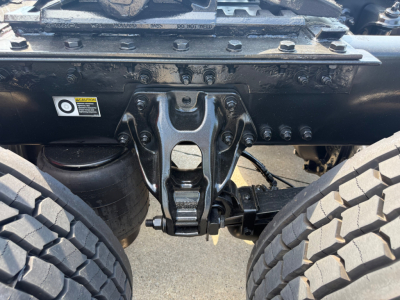 Kenworth T680 chassis view showing rear suspension and hitch assembly in a truck bay; drivetrain mount and dual rear tires visible.