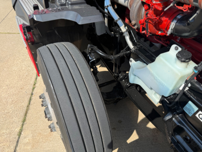 Kenworth T680 engine bay and front wheel area showing coolant reservoir, hoses, and engine components.