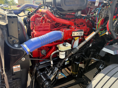 Kenworth T680 engine bay with red Cummins X15 engine, blue intercooler hose, white coolant reservoir, and various wiring harnesses visible.